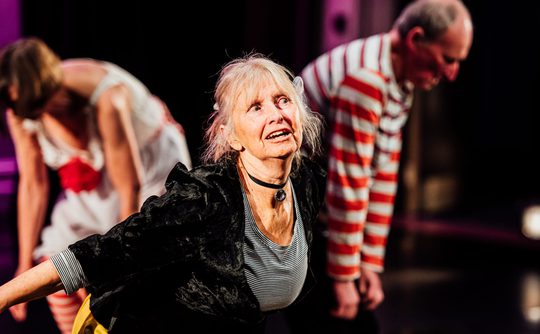 A group of mature performers on stage wearing colourful costumes