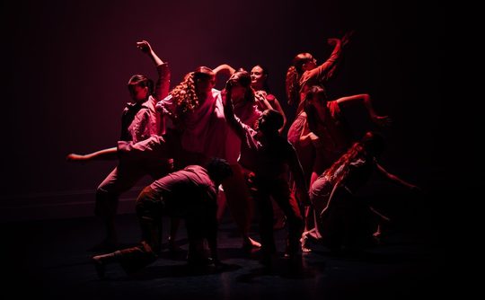 Group of dancers on stage bathed in red light AND WHITE LIGHT