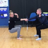 2 dancers in a classroom setting holding hands and leaning away from each other
