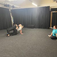2 dancers on the floor in a studio with a black floor and walls