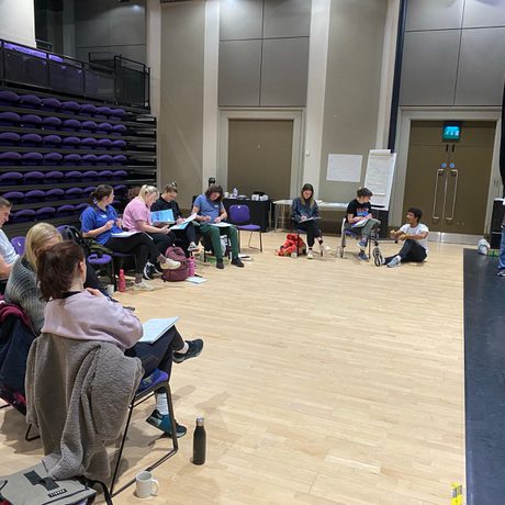 Group of people sat in a semi circle in the theatre looking at papers in their laps
