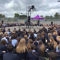 Children sat in a large circle on a playground floor watching a dance performance