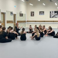 A group of students sat on a dance studio floor in a circle