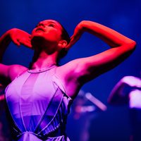 Contemporary dancer with arms on ears, bathed in a pink light