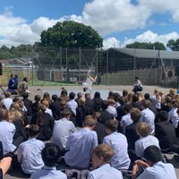 School children sitting in a playground watching a dancer perform