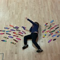 A child lying on the floor in a super hero pose surrounded by colourful feathers
