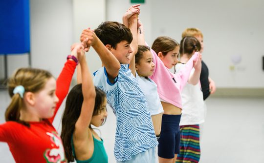 Five children holding hands in a dance studio