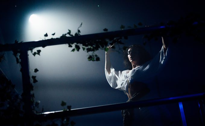 A woman in shade facing a back lit tree on a stage