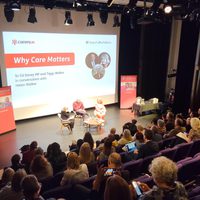 Audience watching a three people sat on stage in front of a large screen