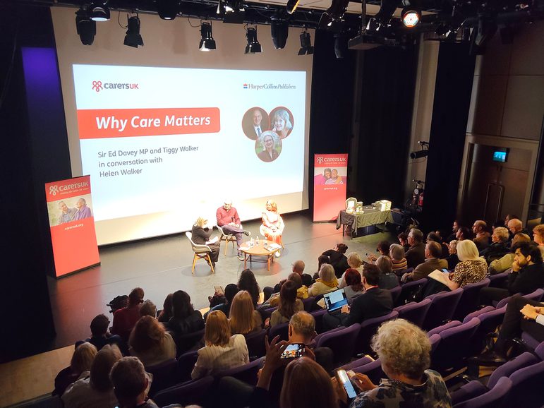 Audience watching a three people sat on stage in front of a large screen