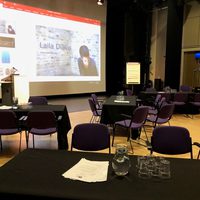 Tables and chairs on stage facing a large projection screen