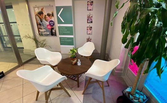 A seating area with a coffee table and 4 white chairs in the foyer area at Pavilion Dance
