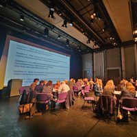 Groups of people sat around tables in the theatre discussing presentation points on a large screen