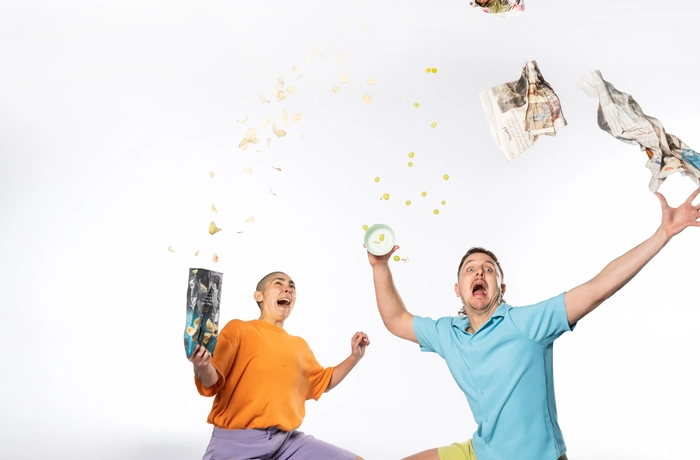 two performers sat on the floor one in an orange top and one in a blue top throwing things in the air