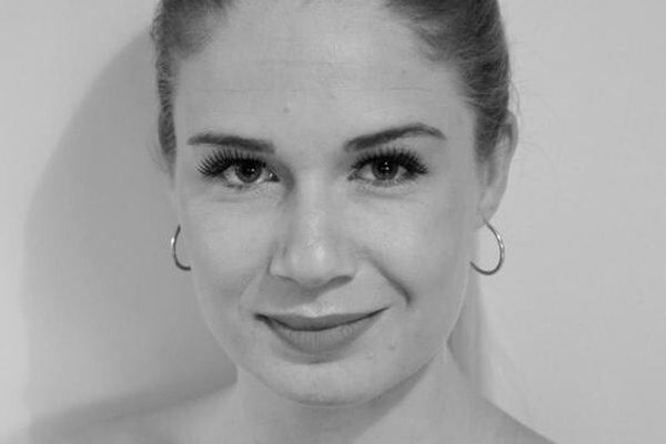 Woman with hair pulled back wearing off the shoulder dark top smiling